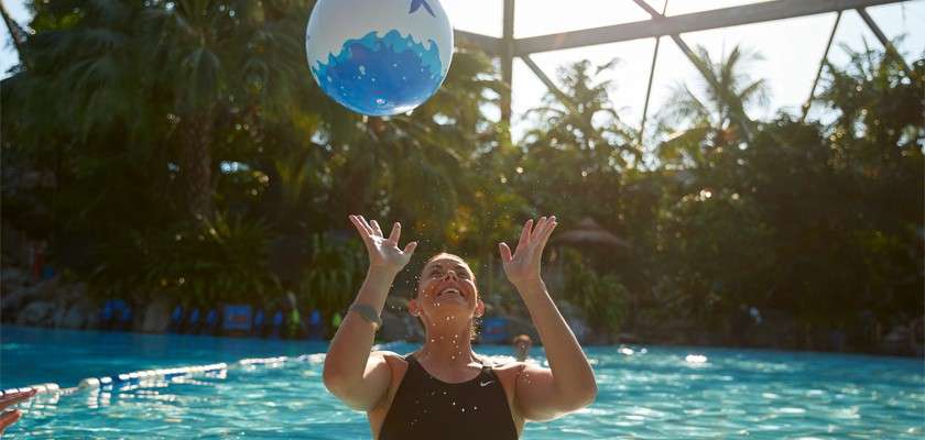 A lady in the Subtropical Swimming Paradise throwing an inflatable ball up into the air. 