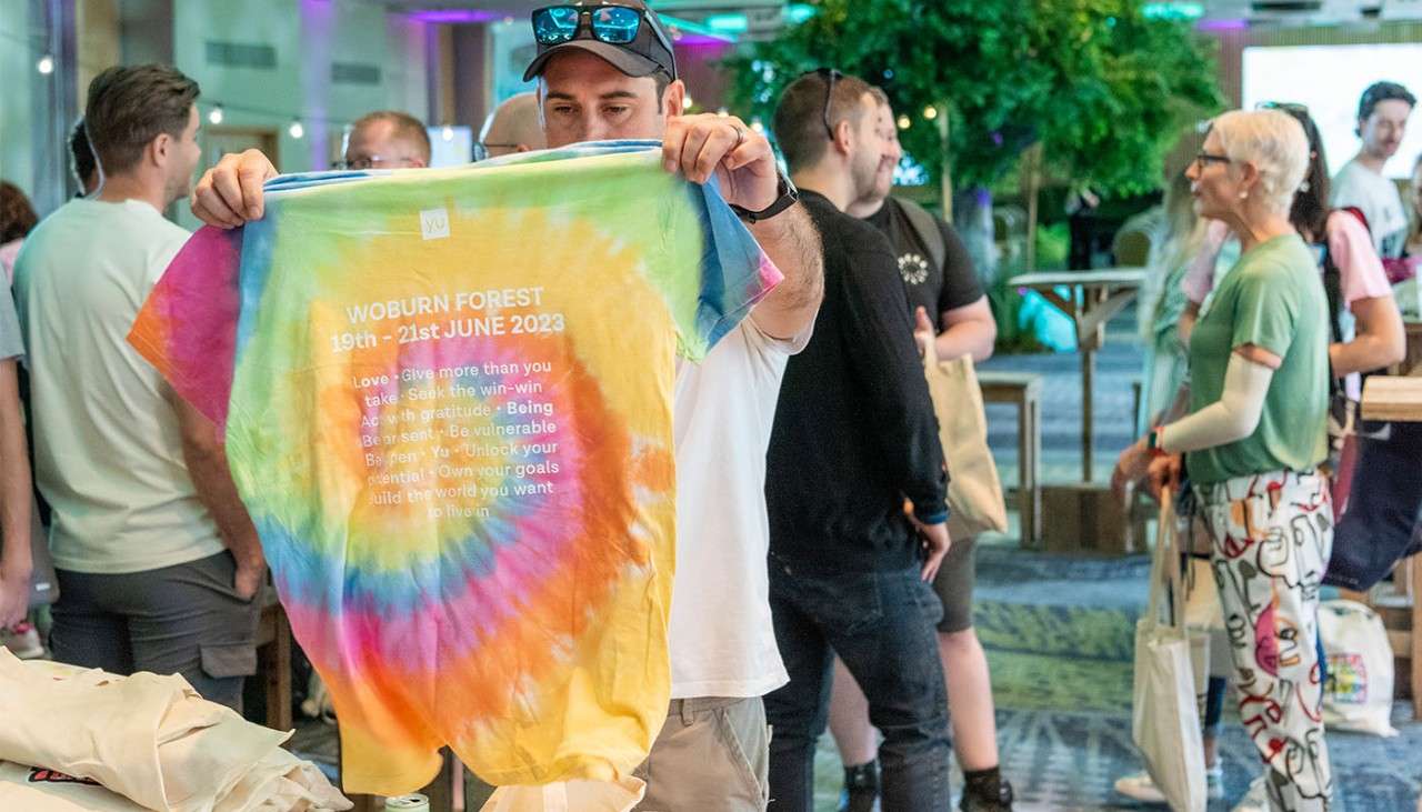 A man holding up a tie-dye t-shirt that says Woburn forest on the back.