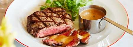 A steak sliced up served with peppercorn sauce and side salad