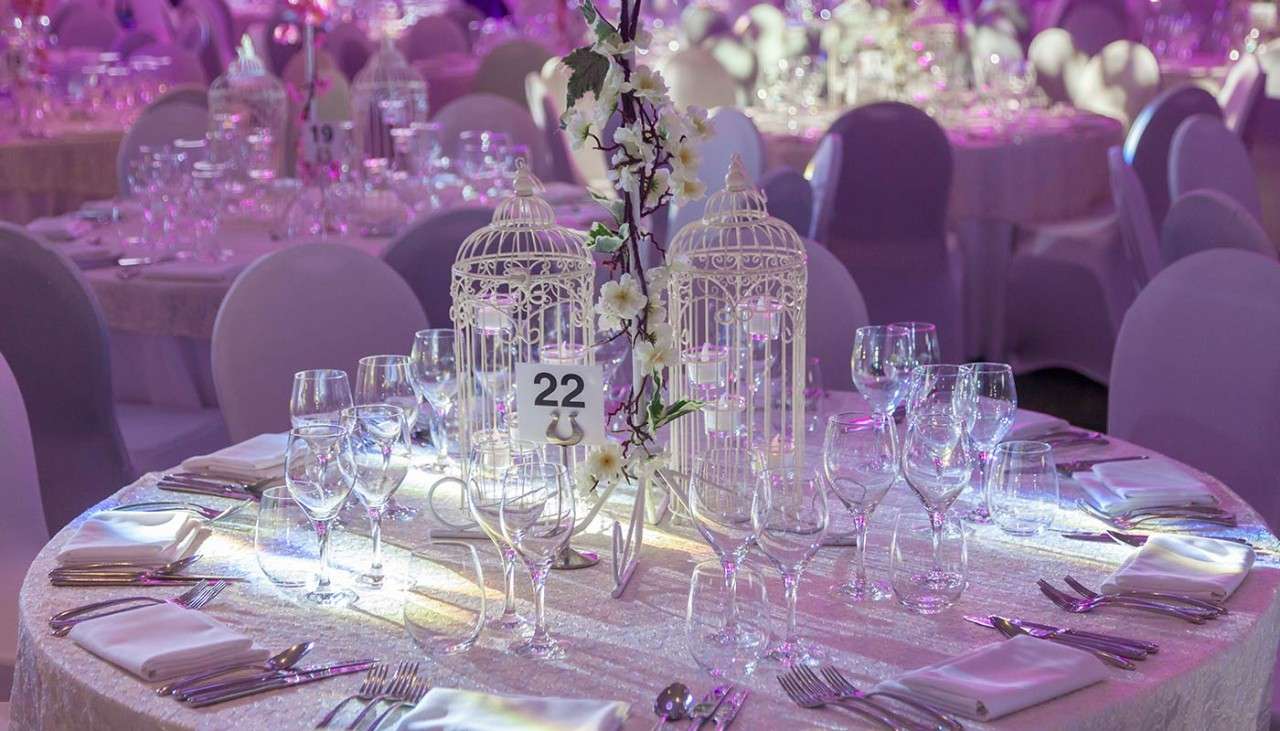 Room decorated with white table cloths and chair covers, with table center pieces of white flowers and birdcages