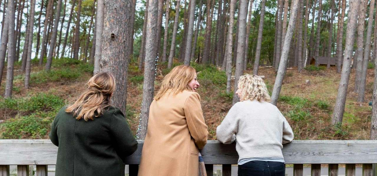 Three delegates standing on the patio of The Venue talking and looking out at the forest.