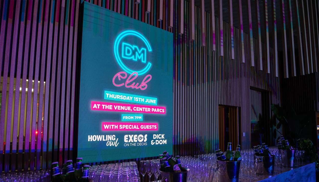 A neon sign about DM club event above a table with drinks glasses on.