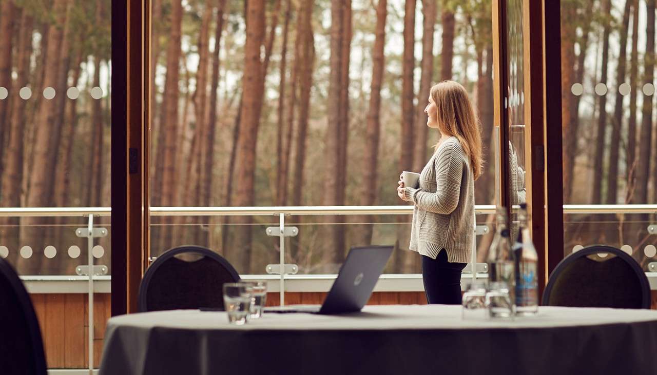 Woman enjoying a cup of tea on a meeting room balcony, taking in the view of the forest